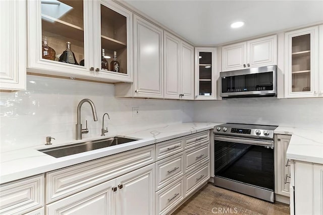 kitchen with sink, dark wood-type flooring, light stone counters, white cabinets, and appliances with stainless steel finishes