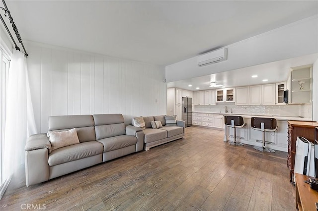 living room with a wall unit AC, wooden walls, dark hardwood / wood-style flooring, and sink