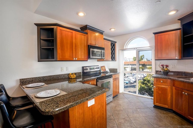 kitchen with kitchen peninsula, a kitchen bar, dark stone counters, a textured ceiling, and stainless steel appliances