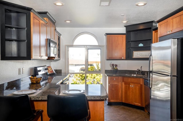 kitchen featuring a textured ceiling, stainless steel appliances, dark tile patterned floors, sink, and dark stone countertops