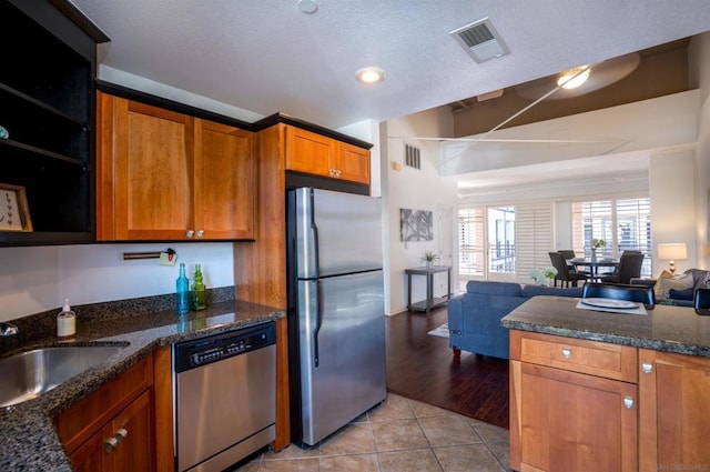 kitchen featuring sink, dark stone counters, a textured ceiling, appliances with stainless steel finishes, and light wood-type flooring