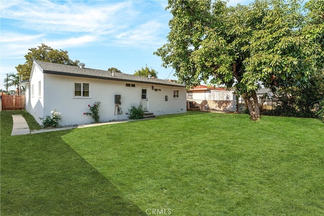 rear view of property with entry steps, a fenced backyard, a lawn, and stucco siding