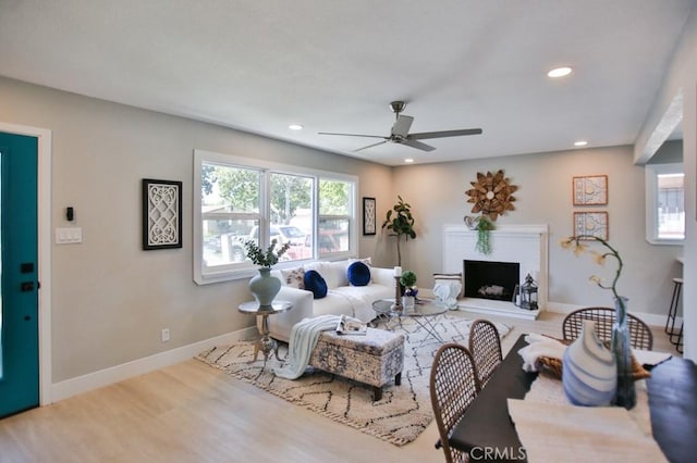 living room featuring baseboards, a fireplace with raised hearth, a ceiling fan, wood finished floors, and recessed lighting