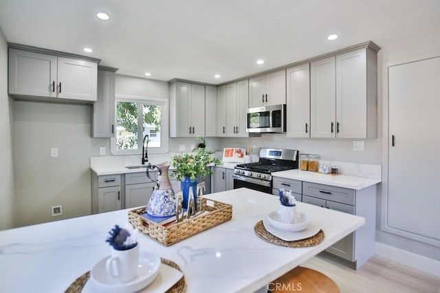 kitchen featuring a breakfast bar, stainless steel appliances, gray cabinetry, a sink, and recessed lighting