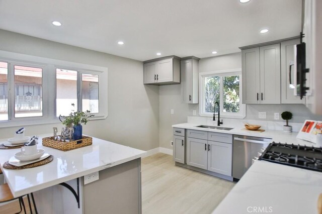 kitchen featuring appliances with stainless steel finishes, light stone countertops, gray cabinetry, a sink, and recessed lighting