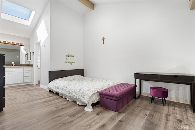 bedroom with light wood-type flooring, a skylight, sink, beam ceiling, and connected bathroom