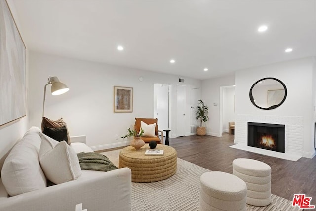 living room featuring a brick fireplace and dark wood-type flooring