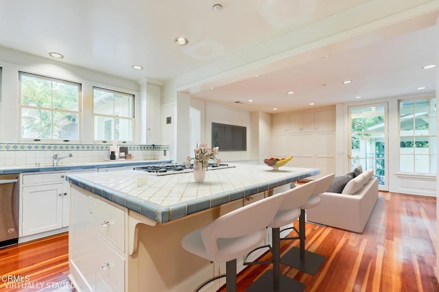 kitchen featuring appliances with stainless steel finishes, light hardwood / wood-style floors, white cabinets, a kitchen bar, and tile countertops