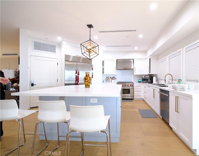 kitchen with decorative light fixtures, premium appliances, wall chimney exhaust hood, and a center island