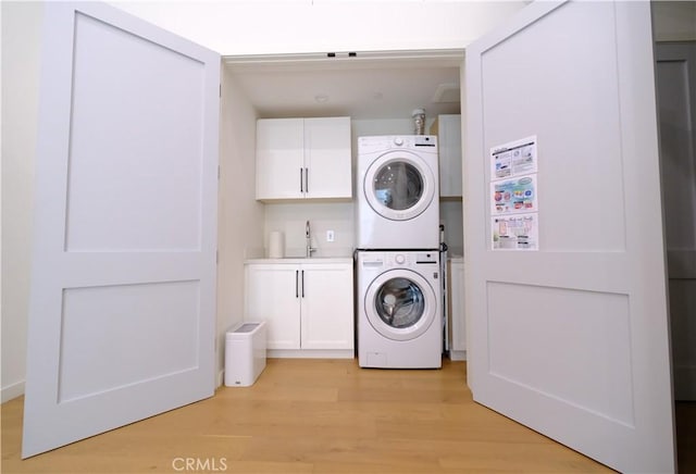 clothes washing area with light hardwood / wood-style floors, cabinets, stacked washer / dryer, and sink