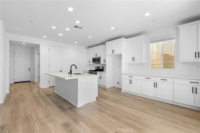 kitchen with decorative backsplash, stainless steel appliances, sink, a center island with sink, and light hardwood / wood-style floors