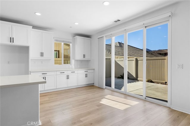 kitchen with decorative backsplash, white cabinetry, and light hardwood / wood-style flooring