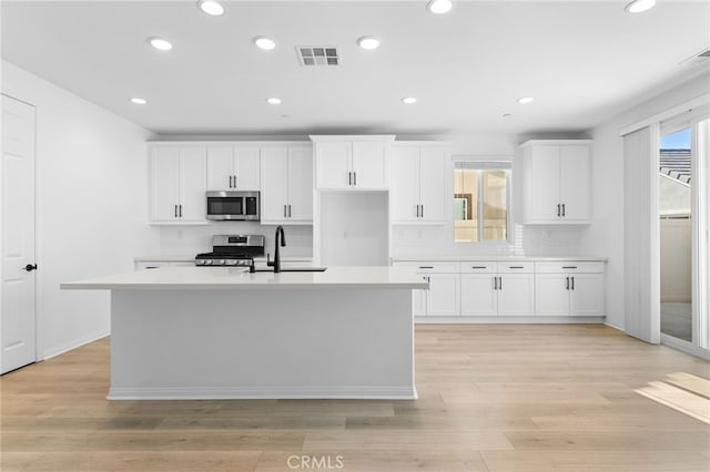 kitchen with white cabinets, light wood-type flooring, a kitchen island with sink, and appliances with stainless steel finishes