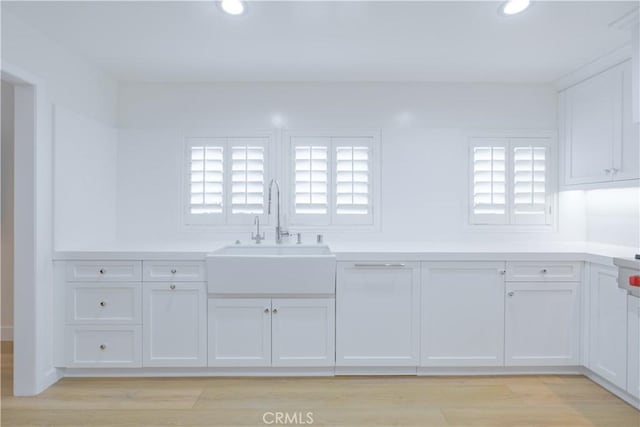 interior space with white cabinets, a healthy amount of sunlight, sink, and light hardwood / wood-style flooring