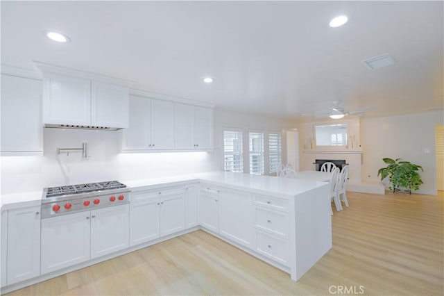 kitchen with white cabinets, kitchen peninsula, light hardwood / wood-style flooring, and stainless steel gas cooktop