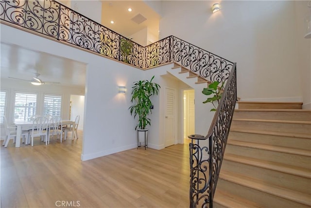 stairs featuring a towering ceiling, hardwood / wood-style flooring, and ceiling fan