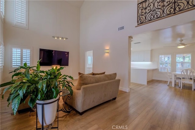 living room featuring ceiling fan, light hardwood / wood-style floors, and a high ceiling