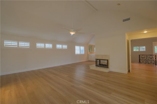 unfurnished living room with ceiling fan, light wood-type flooring, a wealth of natural light, and a tiled fireplace