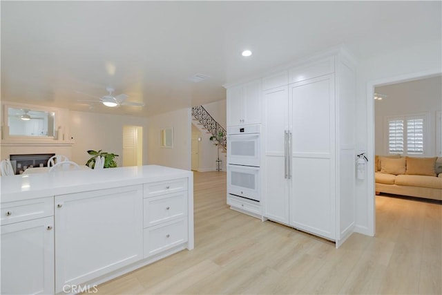 kitchen with light wood-type flooring, white double oven, white cabinetry, and ceiling fan