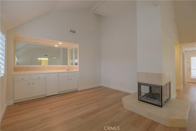 unfurnished living room featuring a multi sided fireplace, sink, high vaulted ceiling, and light hardwood / wood-style flooring