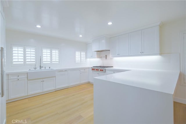 kitchen featuring kitchen peninsula, stainless steel gas cooktop, sink, white cabinets, and light hardwood / wood-style floors