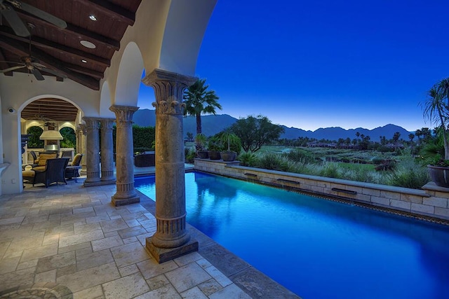 pool at dusk featuring ceiling fan, a mountain view, and a patio