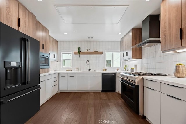 kitchen featuring dark hardwood / wood-style flooring, wall chimney range hood, black appliances, white cabinetry, and plenty of natural light