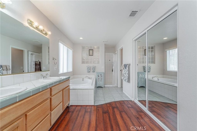 bathroom with hardwood / wood-style floors, vanity, and tiled bath