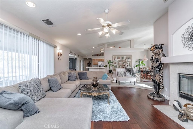 living room featuring hardwood / wood-style flooring, ceiling fan, lofted ceiling, and a tiled fireplace