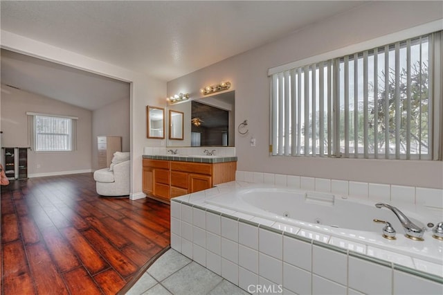 bathroom with hardwood / wood-style floors, vanity, tiled bath, and lofted ceiling