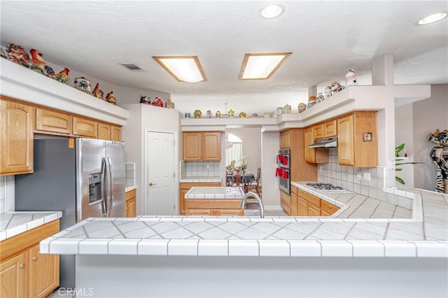 kitchen with kitchen peninsula, tasteful backsplash, stainless steel appliances, sink, and tile counters