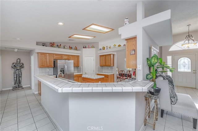 kitchen with tile counters, stainless steel fridge, decorative backsplash, and kitchen peninsula