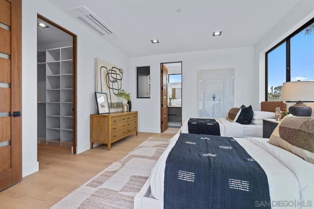 bedroom with connected bathroom, light hardwood / wood-style flooring, and a spacious closet