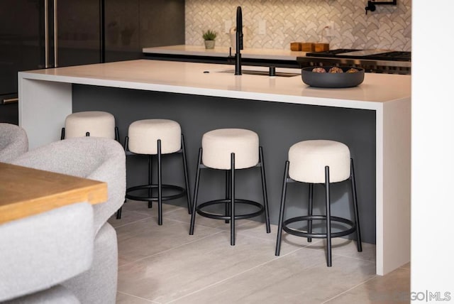 kitchen with sink, light tile patterned flooring, a kitchen bar, and backsplash