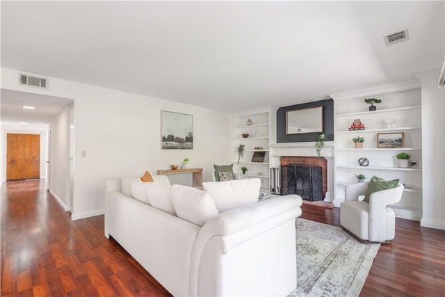 living room featuring built in shelves, a brick fireplace, and dark wood-type flooring