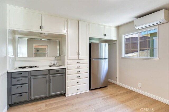 kitchen with a wall mounted air conditioner, white cabinets, sink, stainless steel fridge, and gray cabinets