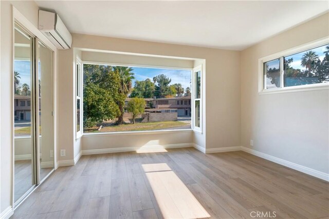 unfurnished room featuring a wall mounted AC, a wealth of natural light, and light hardwood / wood-style flooring