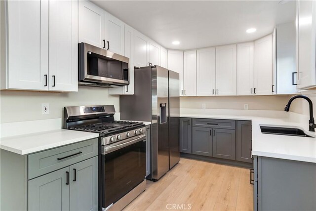 kitchen featuring gray cabinetry, sink, light hardwood / wood-style flooring, white cabinets, and appliances with stainless steel finishes