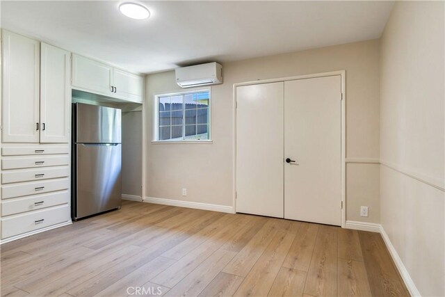 unfurnished bedroom with a wall mounted air conditioner, stainless steel fridge, and light hardwood / wood-style floors