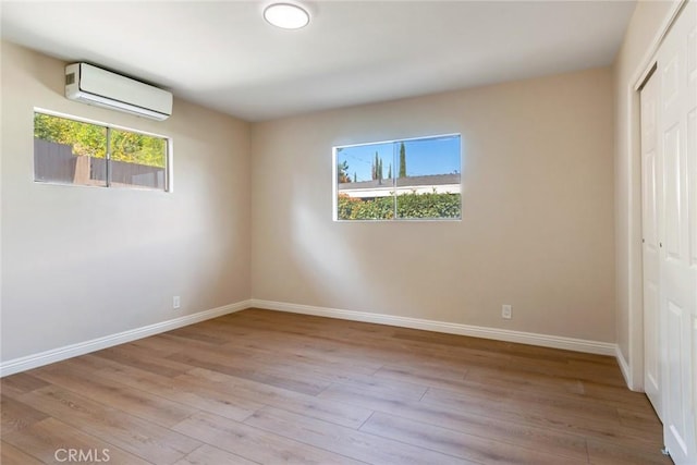 unfurnished bedroom featuring multiple windows, a closet, light hardwood / wood-style flooring, and a wall mounted AC