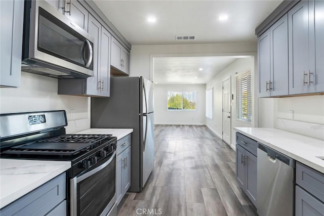 kitchen featuring gray cabinets, light stone countertops, dark wood-type flooring, and appliances with stainless steel finishes