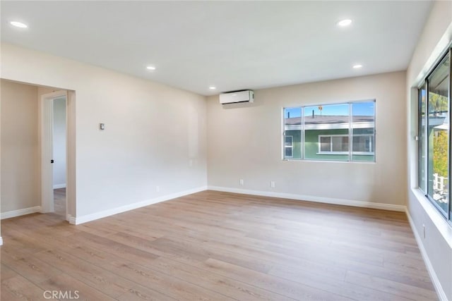 spare room with a wall mounted air conditioner, plenty of natural light, and light hardwood / wood-style flooring