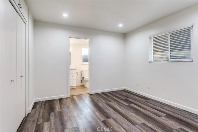 unfurnished bedroom with ensuite bath, dark wood-type flooring, and a closet