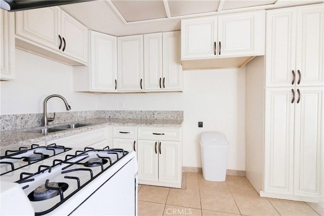 kitchen featuring light stone counters, white range with gas cooktop, sink, light tile patterned floors, and white cabinetry