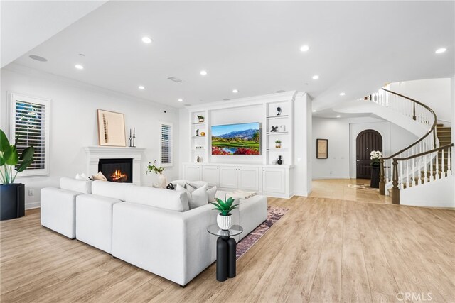 living area with a warm lit fireplace, light wood finished floors, built in features, stairway, and recessed lighting