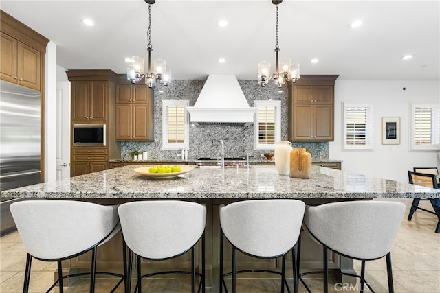 kitchen featuring premium range hood, a large island with sink, and decorative light fixtures