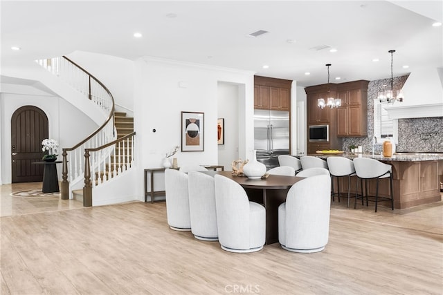 dining space featuring a chandelier, visible vents, light wood finished floors, and stairs