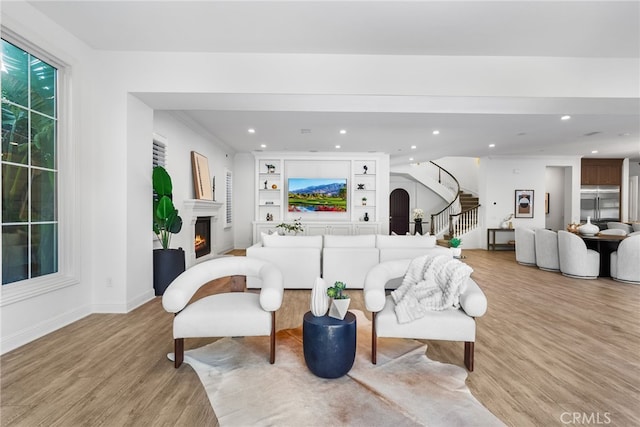 living room featuring built in features, recessed lighting, stairway, light wood-type flooring, and a lit fireplace