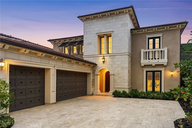 view of front of home with stone siding, decorative driveway, an attached garage, and a balcony