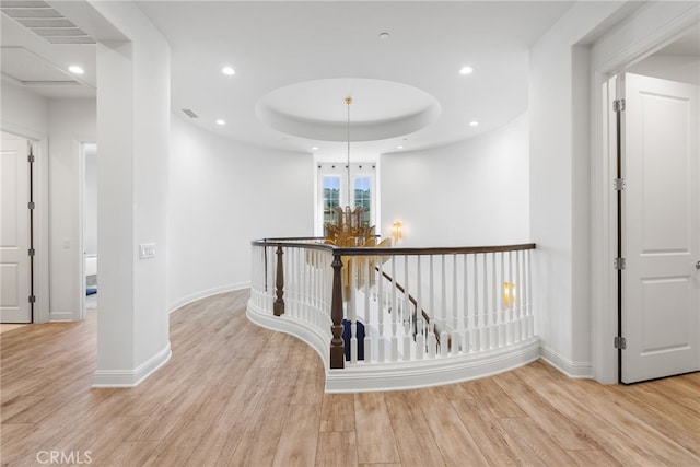 hallway with light wood finished floors, a raised ceiling, an upstairs landing, a notable chandelier, and recessed lighting